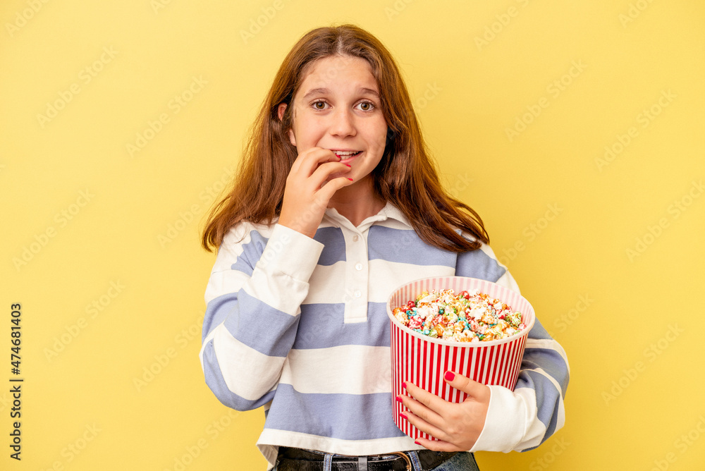 Little caucasian girl holding popcorns isolated on yellow background biting fingernails, nervous and very anxious. Little caucasian girl holding popcorns isolated on yellow background biting fingernails, nervous and very anxious.