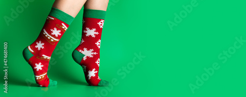 Feet of obscured child in Christmas socks walking on tiptoes against green background