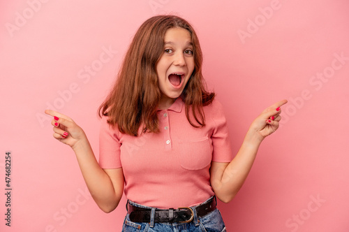 Little caucasian girl isolated on pink background pointing to different copy spaces, choosing one of them, showing with finger.