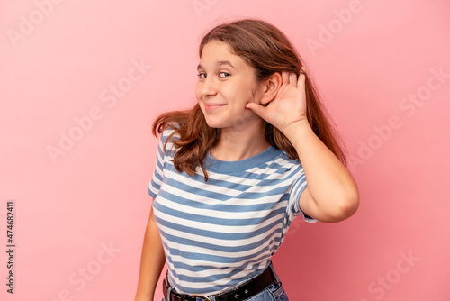 Little caucasian girl isolated on pink background trying to listening a gossip.