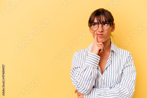 Young Argentinian woman isolated on yellow background looking sideways with doubtful and skeptical expression.