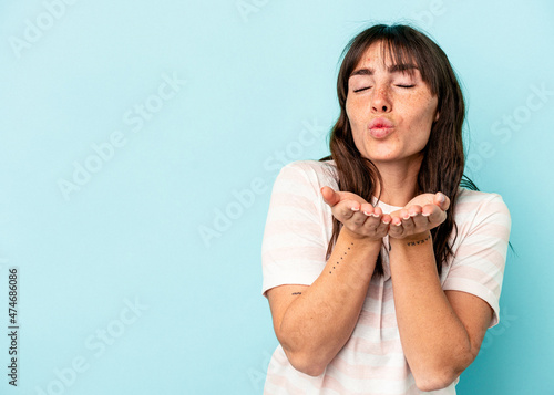Young Argentinian woman isolated on blue background folding lips and holding palms to send air kiss.