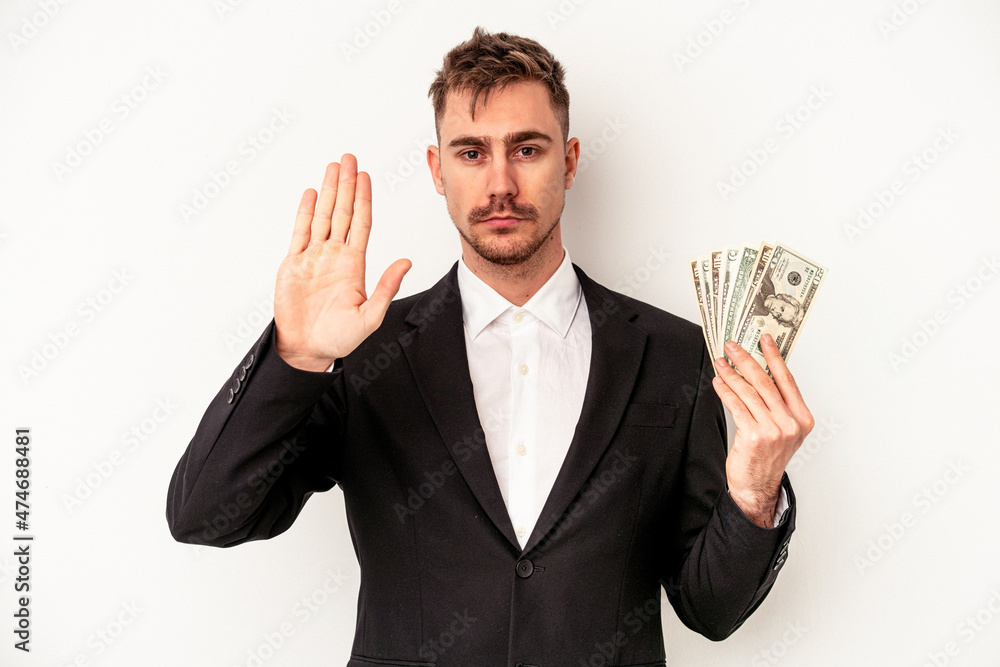 Young caucasian business man holding bank notes isolated on white background standing with outstretched hand showing stop sign, preventing you. Young caucasian business man holding bank notes isolated on white background standing with outstretched hand showing stop sign, preventing you.