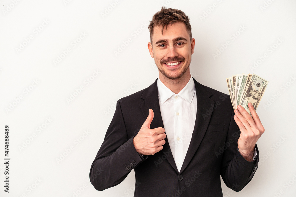 Young caucasian business man holding bank notes isolated on white background smiling and raising thumb up Young caucasian business man holding bank notes isolated on white background smiling and raising thumb up