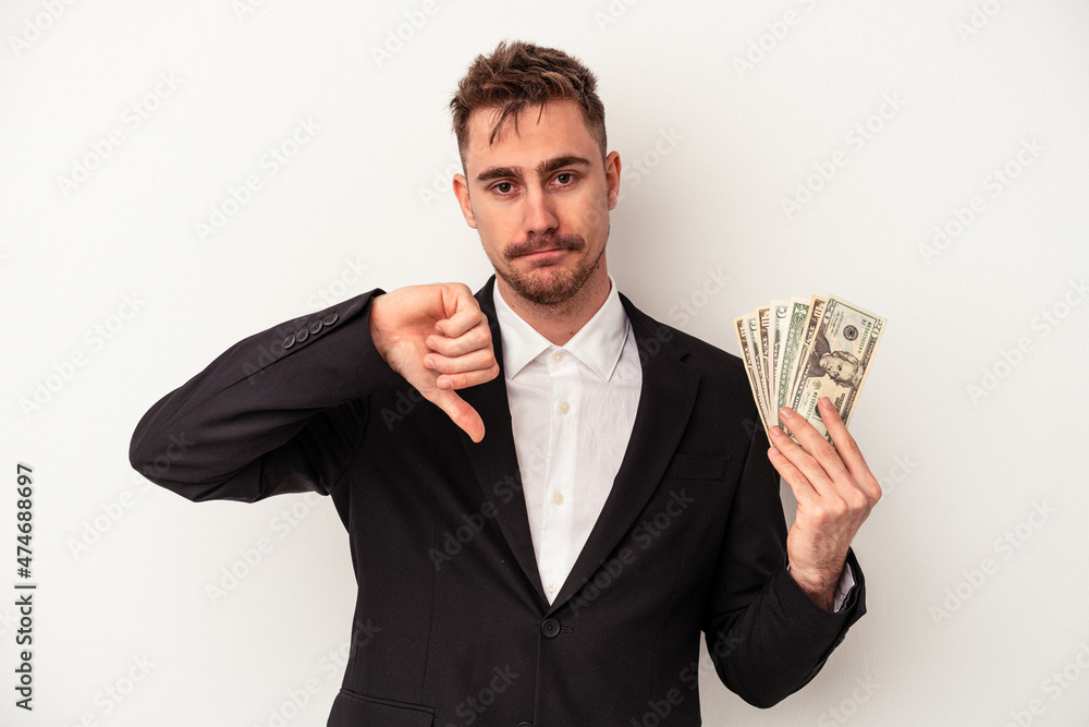 Young caucasian business man holding bank notes isolated on white background showing a dislike gesture, thumbs down. Disagreement concept. Young caucasian business man holding bank notes isolated on white background showing a dislike gesture, thumbs down. Disagreement concept.