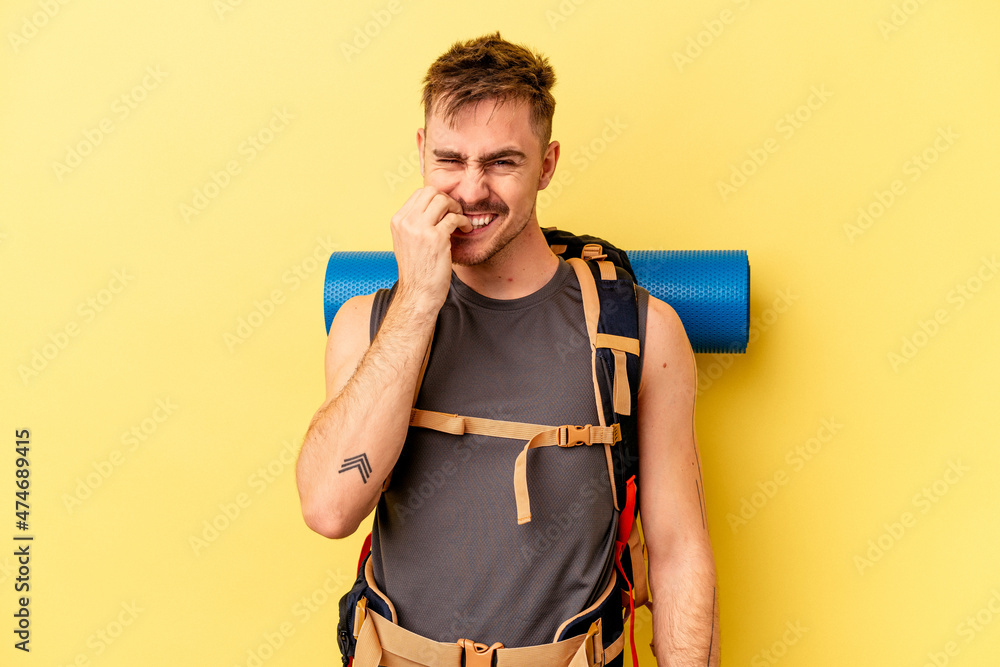 Young hiker caucasian man isolated on yellow background biting fingernails, nervous and very anxious. Young hiker caucasian man isolated on yellow background biting fingernails, nervous and very anxious.