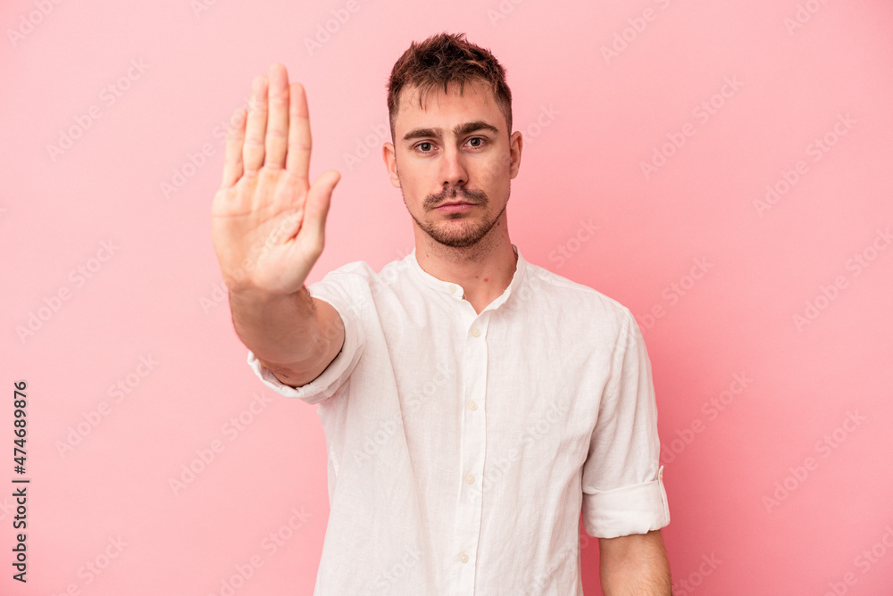 Naklejka premium Young caucasian man isolated on pink background standing with outstretched hand showing stop sign, preventing you.