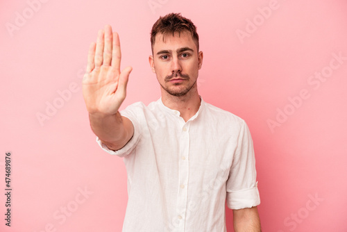 Young caucasian man isolated on pink background standing with outstretched hand showing stop sign, preventing you.