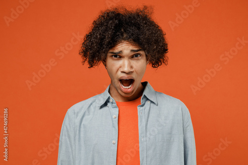 Young disappointed sad displeased offended distempered student black man 50s wearing blue shirt t-shirt look camera isolated on plain orange color background studio portrait. People lifestyle concept. © ViDi Studio