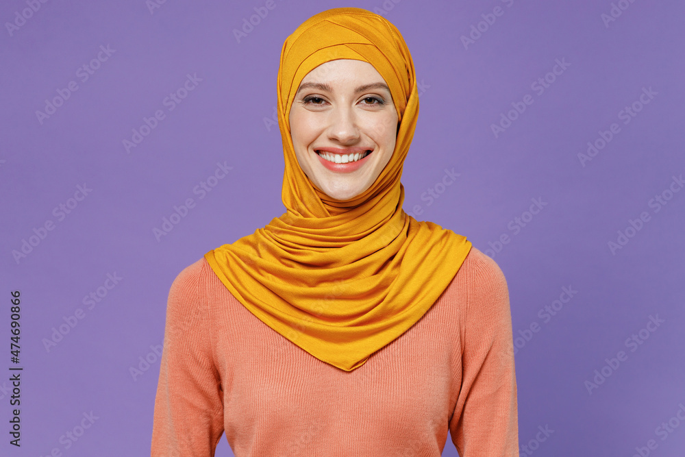 Smiling young arabian asian muslim woman in abaya hijab yellow clothes look camera isolated on plain pastel light violet background studio portrait. People uae middle eastern islam religious concept. Smiling young arabian asian muslim woman in abaya hijab yellow clothes look camera isolated on plain pastel light violet background studio portrait. People uae middle eastern islam religious concept.
