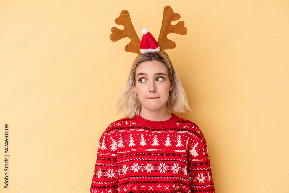 Young caucasian woman wearing a christmas reindeer hat isolated on yellow background confused, feels doubtful and unsure. Young caucasian woman wearing a christmas reindeer hat isolated on yellow background confused, feels doubtful and unsure.