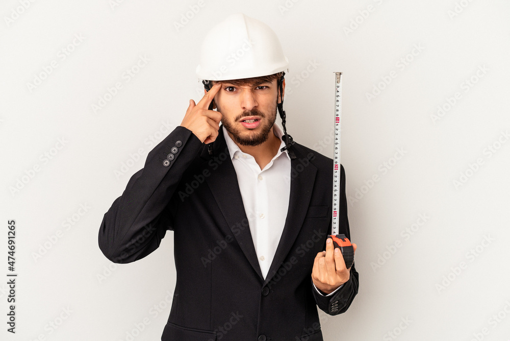 Young mixed race architect man wearing a helmet and holding meter isolated on grey background showing a disappointment gesture with forefinger. Young mixed race architect man wearing a helmet and holding meter isolated on grey background showing a disappointment gesture with forefinger.