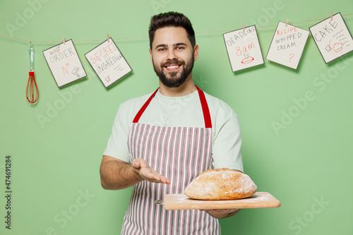 Photography Young fun smiling happy male chef confectioner baker man 20s in striped apron hold point hand on warm homemade bread look camera isolated on plain pastel light green background