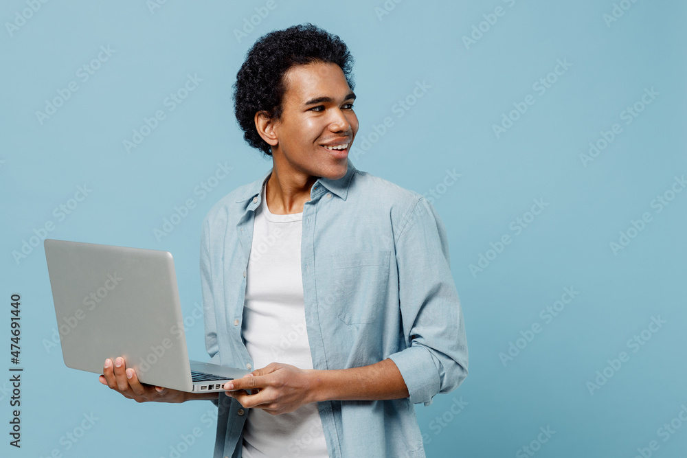 Fascinating excited delight young black curly man 20s years old wear white shirt hold use work on laptop pc computer looking back behind isolated on plain pastel light blue background studio portrait Fascinating excited delight young black curly man 20s years old wear white shirt hold use work on laptop pc computer looking back behind isolated on plain pastel light blue background studio portrait