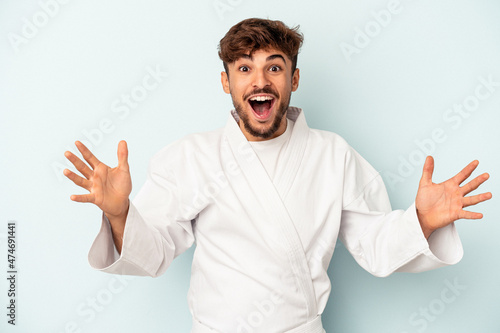Young mixed race man doing karate isolated on blue background receiving a pleasant surprise, excited and raising hands.