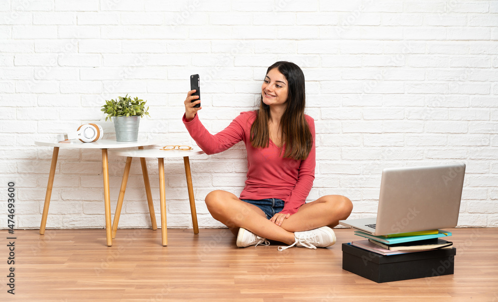 Young woman with a laptop sitting on the floor at indoors making a selfie Young woman with a laptop sitting on the floor at indoors making a selfie