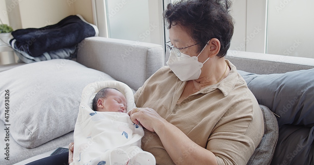 Happy Asian Grandmother with protective face mask holding cute lovely little newborn baby infant in arms at living room at home, Happiness Parent and Newborn Baby at Comfortable Home in Day Lighting	
