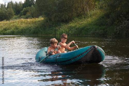 Two children ride a rubber boat on the river on a summer day. © ksi