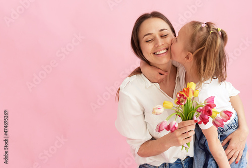 The daughter gives her mother a bouquet of flowers and kisses her on the cheek. Mother's day concept, mother and daughter love