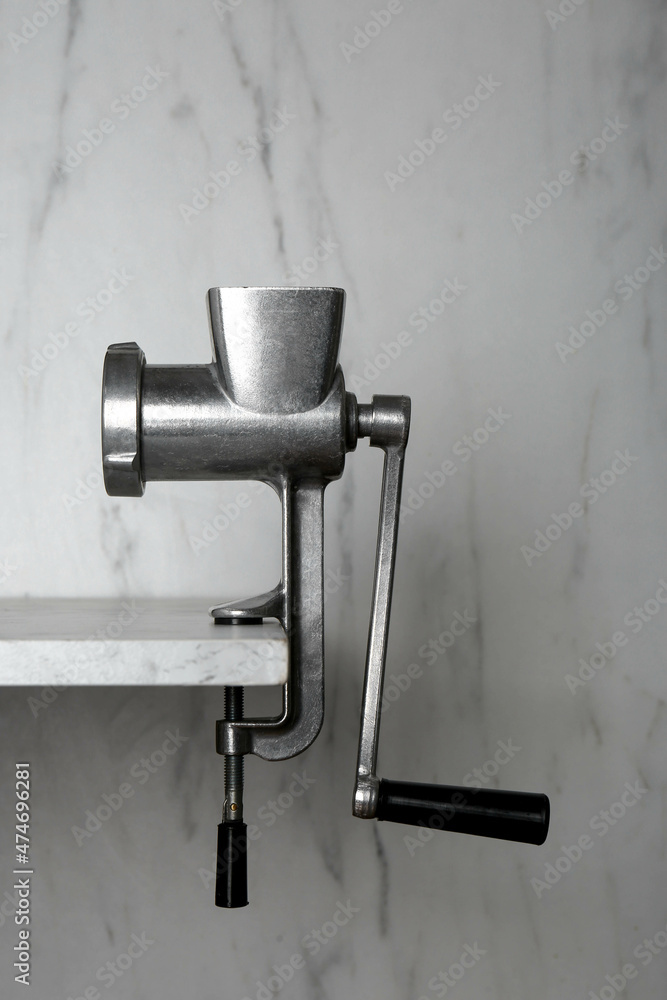Metal manual meat grinder on table against white marble background Metal manual meat grinder on table against white marble background