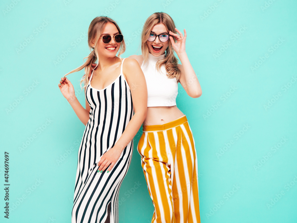 Two young beautiful smiling brunette hipster female in trendy summer clothes. carefree women posing near blue wall in studio. Positive models having fun. Cheerful and happy