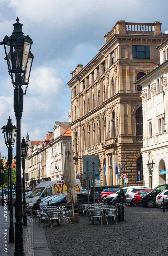 A classic street architecture. A street in the historic city center of Prague, Czech Republic, with a classic flat-roofed building, black lampposts and a somewhat overcast sky. The street is paved. 