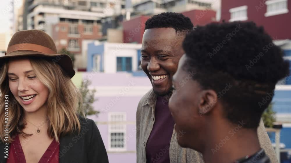 Black male and multi-ethnic group of adult friends socializing on a rooftop in the city. Smiling and laughing at a party Black male and multi-ethnic group of adult friends socializing on a rooftop in the city. Smiling and laughing at a party