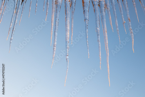 beautiful icicles shine in sun against blue sky. spring landscape with ice icicles hanging from roof of house.