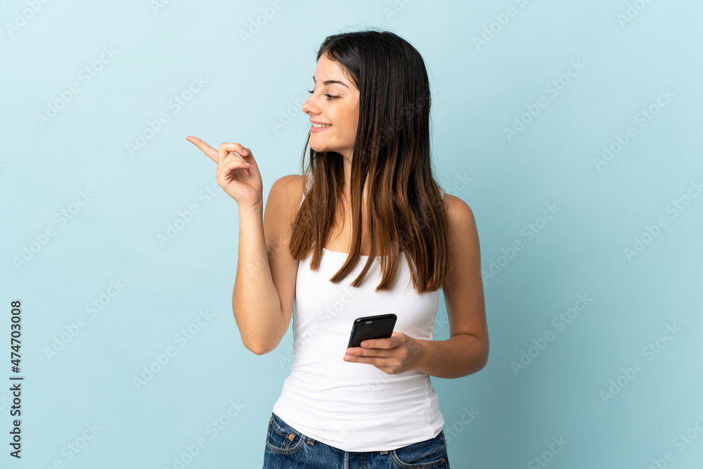 Young caucasian woman using mobile phone isolated on blue background intending to realizes the solution while lifting a finger up Young caucasian woman using mobile phone isolated on blue background intending to realizes the solution while lifting a finger up