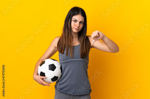 Young football player woman isolated on yellow background showing thumb down with negative expression © luismolinero