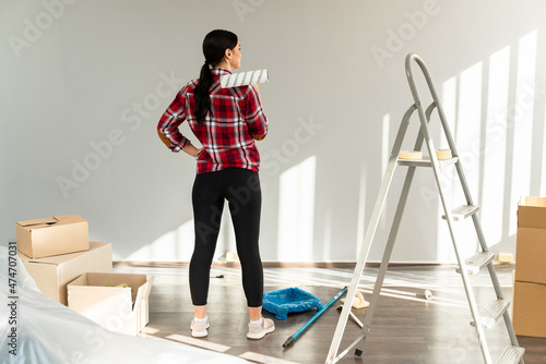 Rear view shot of a casual brunette woman looking at the walls while painting her living room at new apartments
