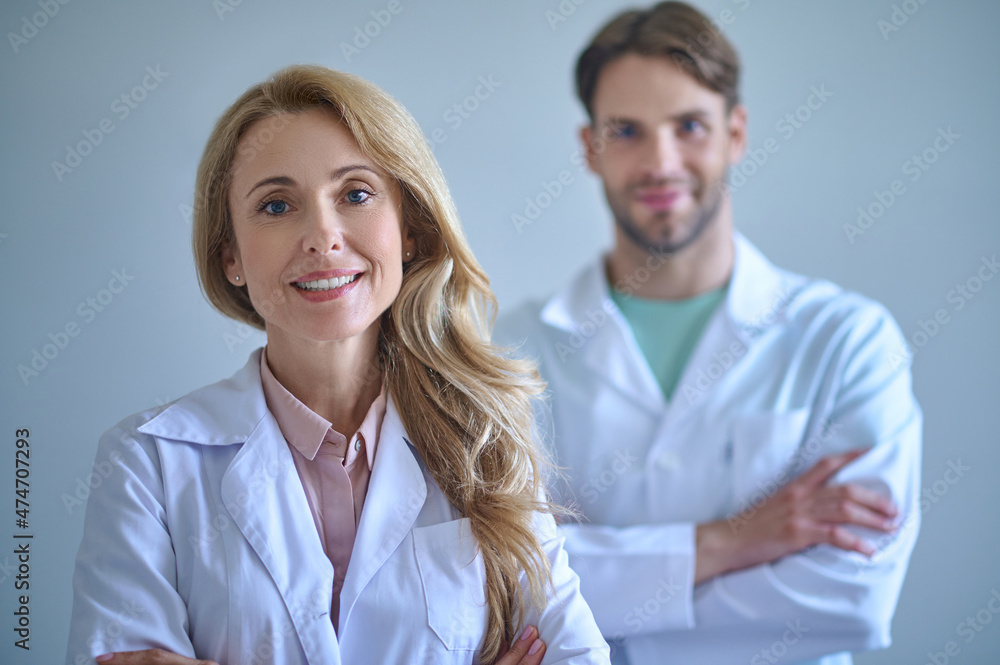Woman in white coat looking at camera and colleague Woman in white coat looking at camera and colleague