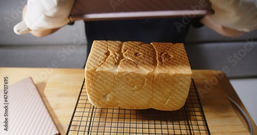 Woman taking out Fresh homemade Baked Japanese Soft and Fluffy Bun loaf of Bread or shokupan bread from toast mold box bread, Popular as Hokkaido Milk Bread at home kitchen photo