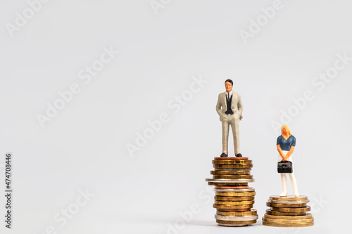 Miniature successful businessmen are standing on stacks of coins. A man and a woman in business, the difference in salary and positions, the concept of infringement of women's rights and feminism