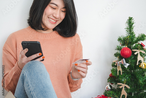 young woman sit on floor, using mobile phone, and holding credit card for christmas online shopping