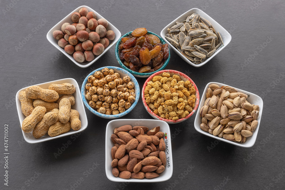 Almond in selective focus. Dried mulberry, hazelnut, pistachio, grape, pistachio, yellow chickpea and sunflower seeds in the background. Almond in selective focus. Dried mulberry, hazelnut, pistachio, grape, pistachio, yellow chickpea and sunflower seeds in the background.