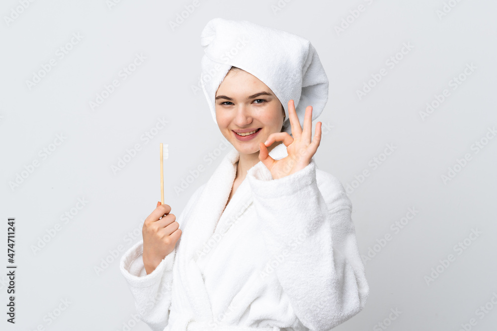 Young woman in a bathrobe holding toothbrush showing ok sign with fingers Young woman in a bathrobe holding toothbrush showing ok sign with fingers