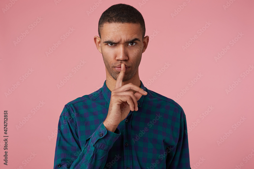 studio portrait of middle age middle eastern man wears blue checkered shirt shows silence gesture with angry facial expression, raised up eyebrow, isolated over pink background studio portrait of middle age middle eastern man wears blue checkered shirt shows silence gesture with angry facial expression, raised up eyebrow, isolated over pink background
