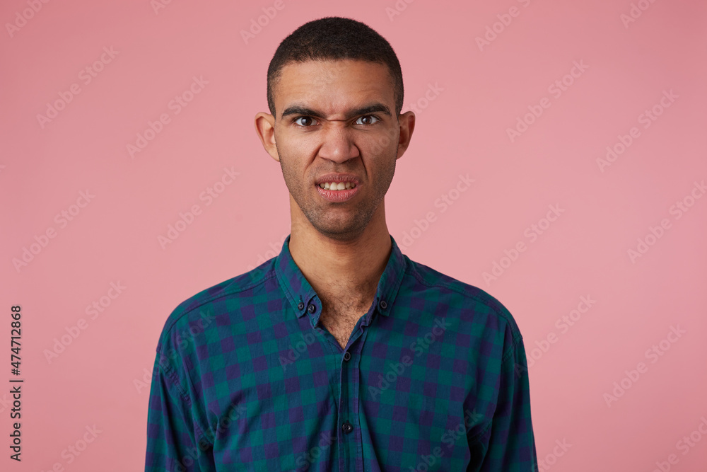 studio portrait of middle age middle eastern man wears blue checkered shirt grin with angry facial expression. isolated over pink background studio portrait of middle age middle eastern man wears blue checkered shirt grin with angry facial expression. isolated over pink background