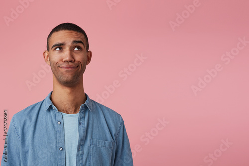 studio portrait of middle age middle eastern man wears blue shirt confused looking aside at copy space. isolated over pink background