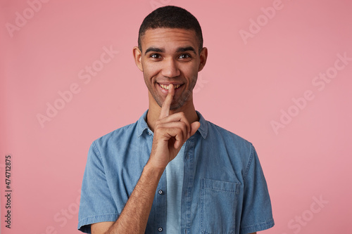 studio portrait of middle age middle eastern man wears blue shirt flirting and shows silence gesture, isolated over pink background