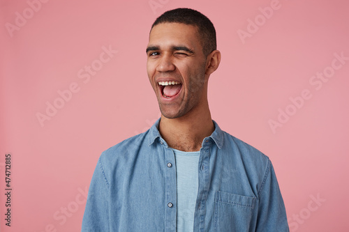 studio portrait of middle age middle eastern man wears blue shirt wink with positive glad facial expression. isolated over pink background