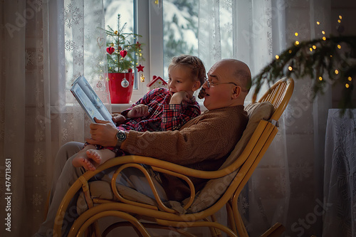 grandfather sitting in a chair and reading a fairy tale to his granddaughter on Christmas eve photo