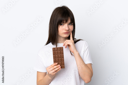 Young Ukrainian woman isolated on white background taking a chocolate tablet and having doubts