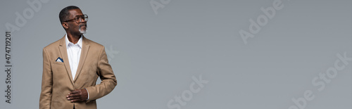 senior african american businessman in formal wear and eyeglasses looking away isolated on grey, banner