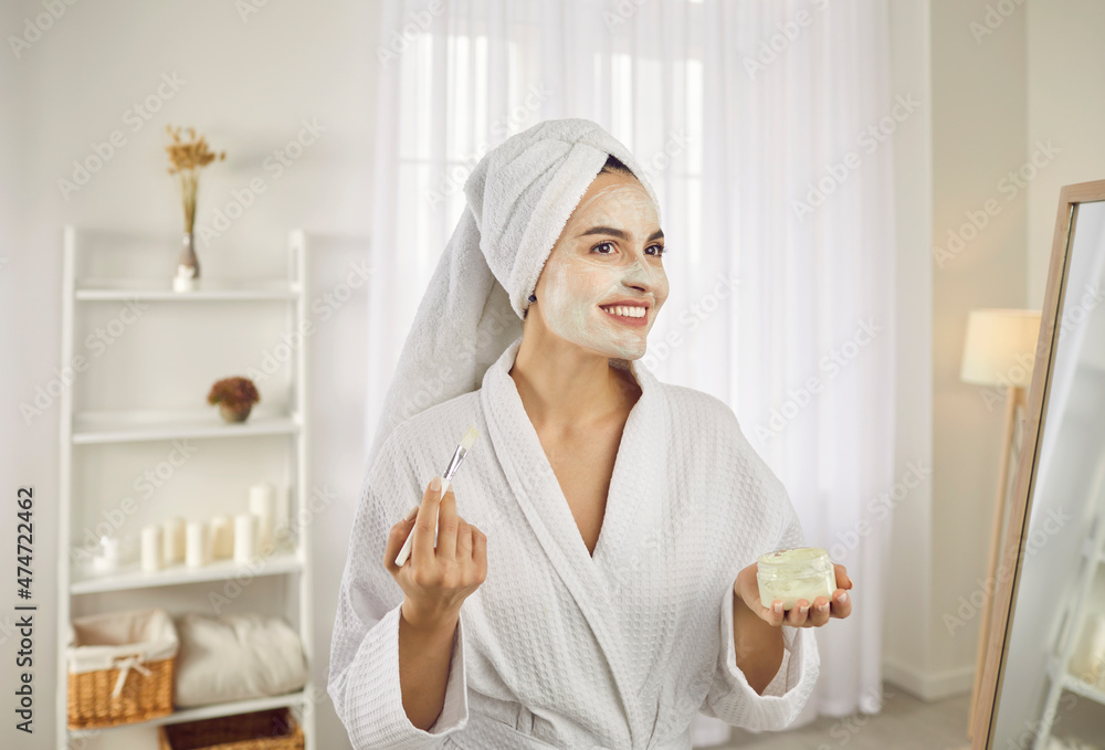 Beauty treatments at home. Beautiful woman in morning applies moisturizing mask or cream on face with brush. Portrait of beautiful woman in bathrobe and towel. Concept of skin care and lifestyle. Beauty treatments at home. Beautiful woman in morning applies moisturizing mask or cream on face with brush. Portrait of beautiful woman in bathrobe and towel. Concept of skin care and lifestyle.