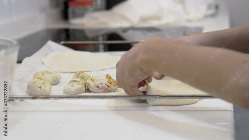 Child's hands placing pizza dough on the oven tray next to the filled dough bags. Selective focus Child's hands placing pizza dough on the oven tray next to the filled dough bags. Selective focus
