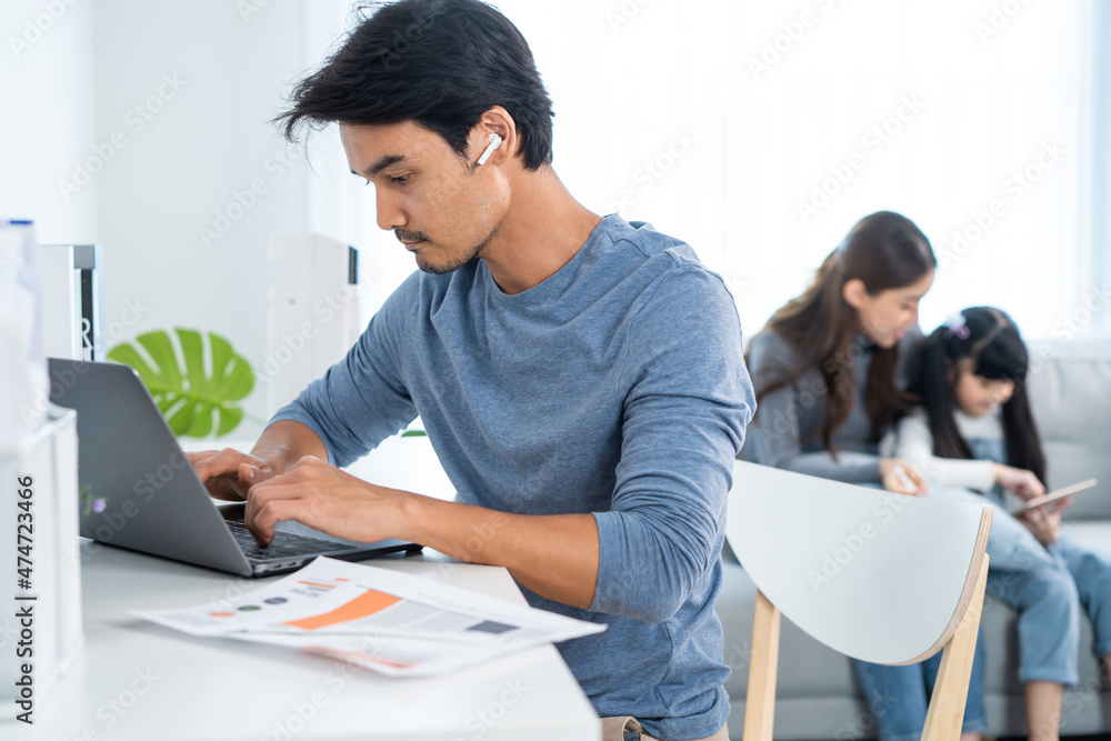 Asian business man father sit on table work at home with family behind Asian business man father sit on table work at home with family behind