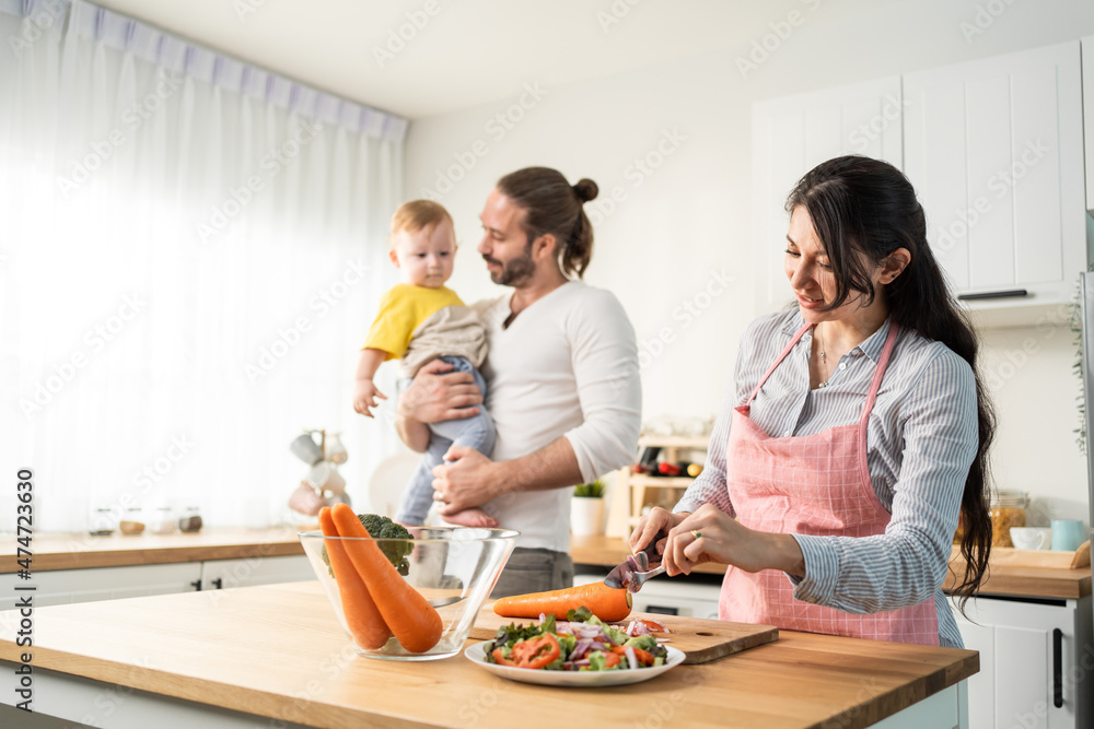 Caucasian beautiful parents cook food with baby boy toddler in kitchen Caucasian beautiful parents cook food with baby boy toddler in kitchen