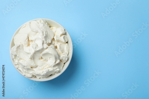 Bowl of tasty cream cheese on light blue background  top view. Space for text